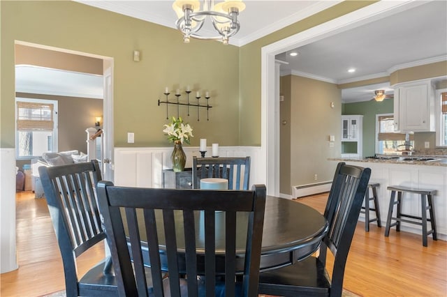 dining area with a wainscoted wall, ornamental molding, baseboard heating, and light wood-style flooring