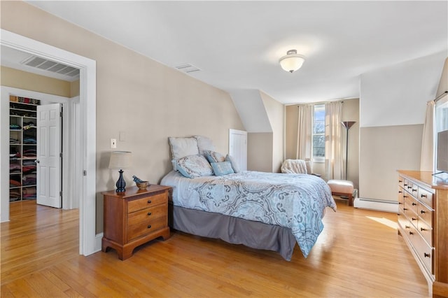 bedroom with light wood-style flooring, visible vents, vaulted ceiling, a spacious closet, and baseboard heating