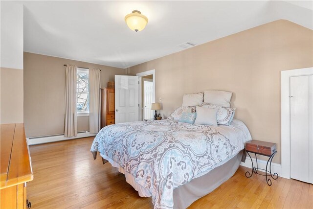 bedroom with baseboards, visible vents, lofted ceiling, a baseboard radiator, and wood finished floors