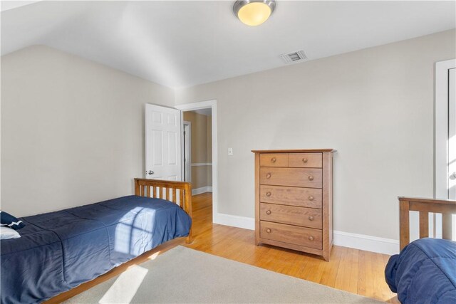 bedroom featuring vaulted ceiling, wood finished floors, visible vents, and baseboards