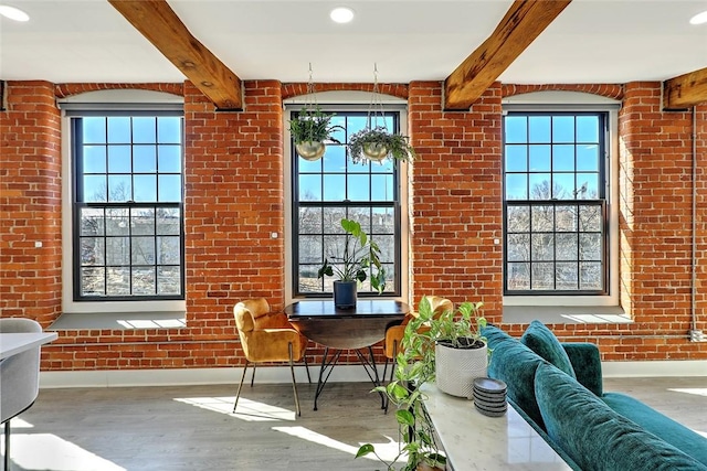 interior space featuring baseboards, beamed ceiling, brick wall, and wood finished floors