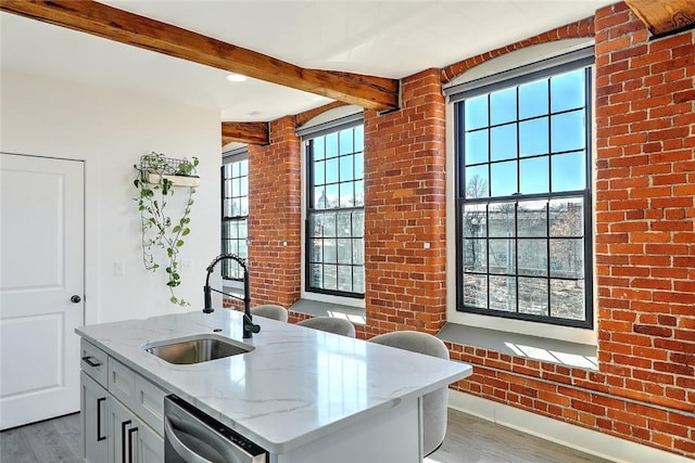 kitchen featuring light stone counters, beamed ceiling, wood finished floors, a sink, and stainless steel dishwasher