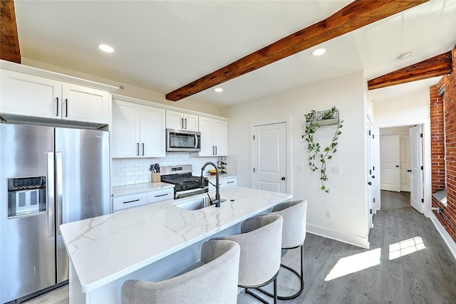 kitchen featuring light wood-style flooring, stainless steel appliances, a sink, backsplash, and beamed ceiling