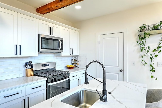 kitchen with backsplash, appliances with stainless steel finishes, white cabinetry, a sink, and beamed ceiling