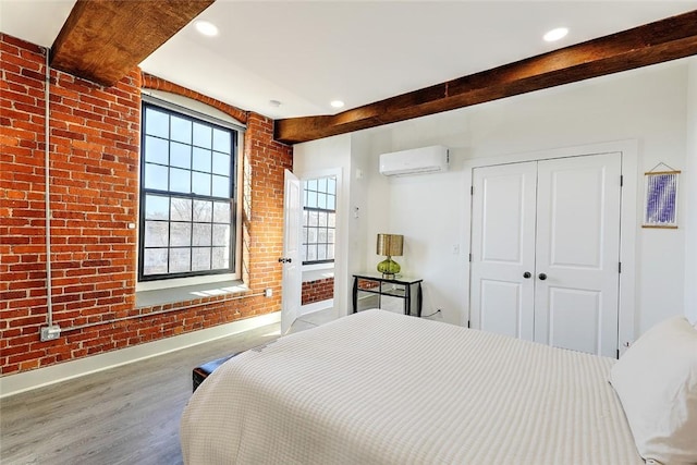 bedroom featuring brick wall, wood finished floors, a wall mounted AC, a closet, and beam ceiling