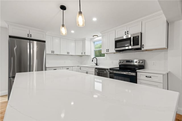 kitchen featuring light wood finished floors, decorative backsplash, appliances with stainless steel finishes, white cabinetry, and a sink