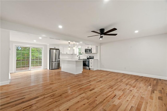 kitchen featuring stainless steel appliances, light countertops, light wood-style floors, open floor plan, and white cabinetry