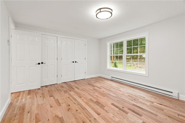 unfurnished bedroom featuring baseboards, baseboard heating, two closets, and light wood-style floors