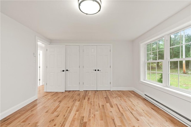 unfurnished bedroom with baseboards, light wood-style flooring, a baseboard heating unit, and multiple closets