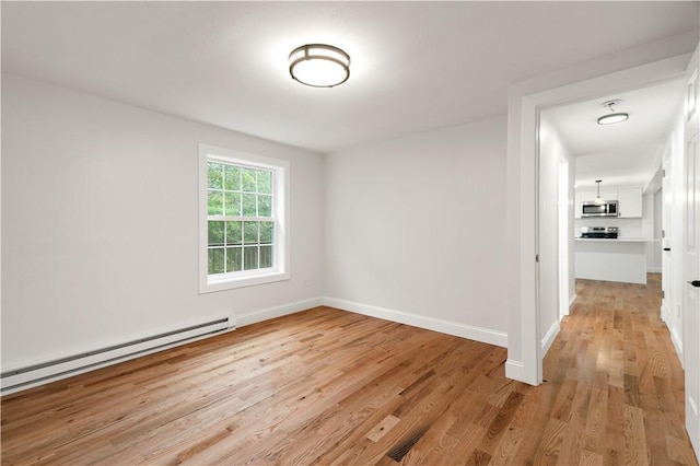 unfurnished room with baseboard heating, light wood-type flooring, and baseboards