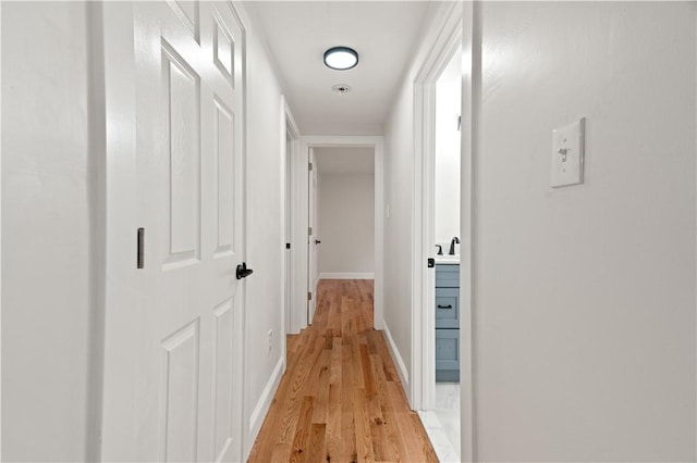 hallway with light wood-type flooring, a sink, and baseboards