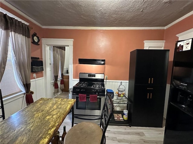 kitchen featuring wainscoting, ornamental molding, stainless steel gas range, a textured ceiling, and exhaust hood