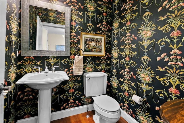 half bathroom with toilet, wallpapered walls, baseboards, and wood finished floors