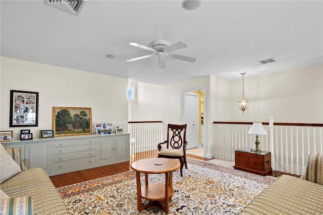 living area featuring ceiling fan with notable chandelier, visible vents, and wood finished floors