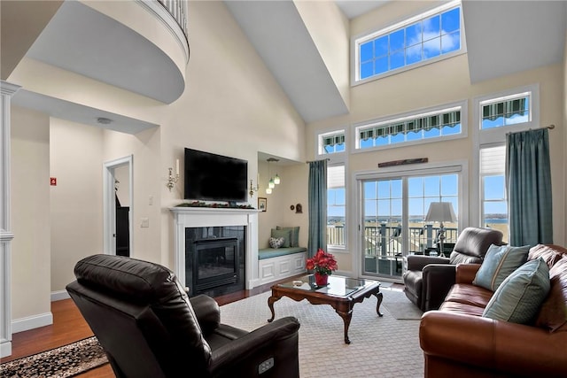 living room featuring baseboards, a towering ceiling, a tiled fireplace, and wood finished floors