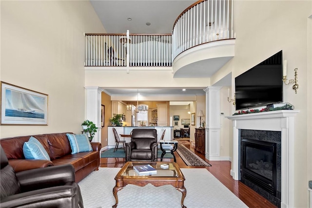 living room featuring a notable chandelier, dark wood-type flooring, a high ceiling, a glass covered fireplace, and decorative columns