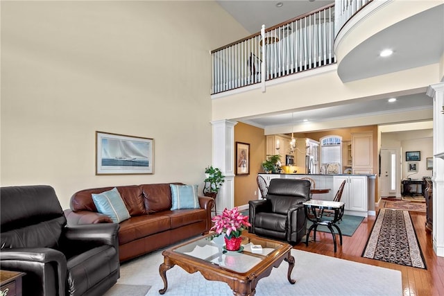 living room featuring light wood-style flooring, recessed lighting, a high ceiling, ornamental molding, and ornate columns