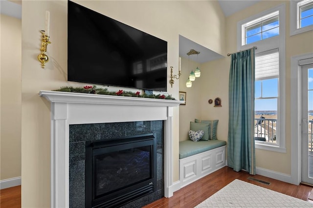 living area featuring wood finished floors, a glass covered fireplace, visible vents, and baseboards