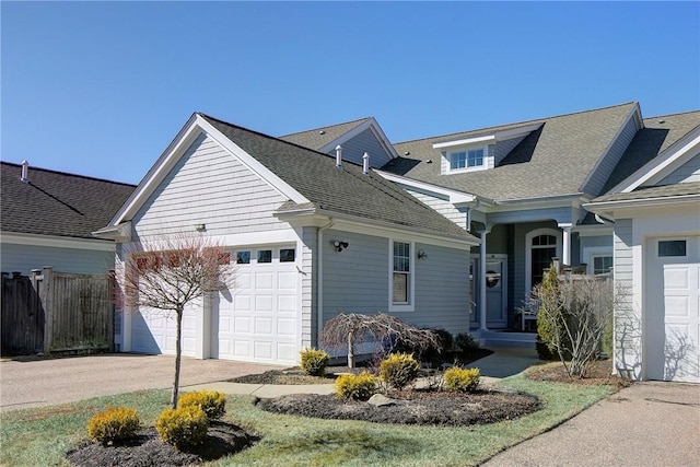 view of front facade featuring driveway, roof with shingles, an attached garage, and fence