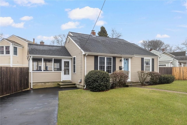 view of front of property with a sunroom, roof with shingles, a front yard, and fence