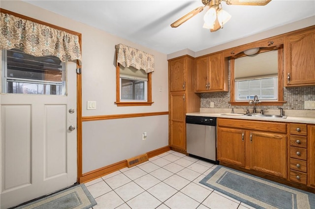 kitchen featuring a sink, backsplash, stainless steel dishwasher, brown cabinetry, and light countertops