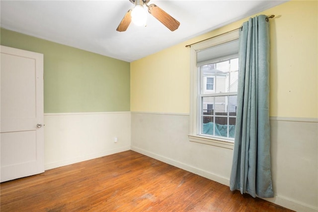 spare room featuring a ceiling fan, wood finished floors, a healthy amount of sunlight, and baseboards