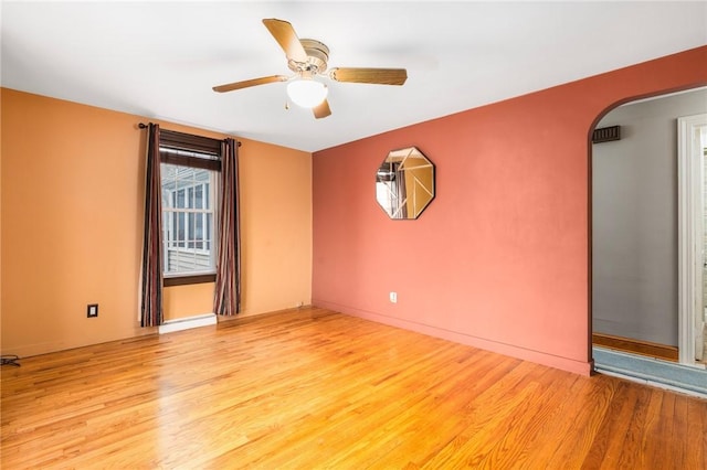 empty room featuring light wood-style flooring, baseboards, arched walkways, and ceiling fan