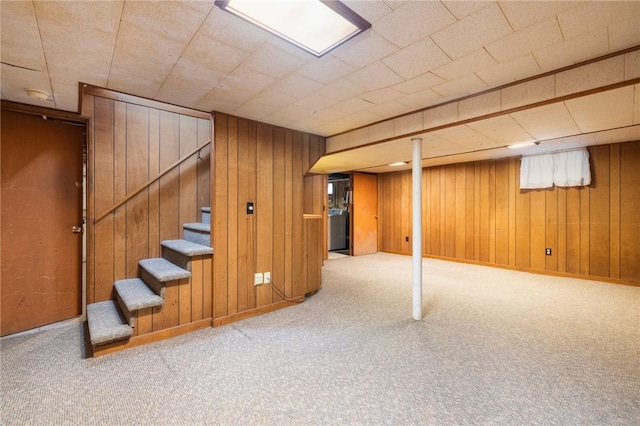 finished below grade area featuring baseboards, carpet floors, wooden walls, and stairs