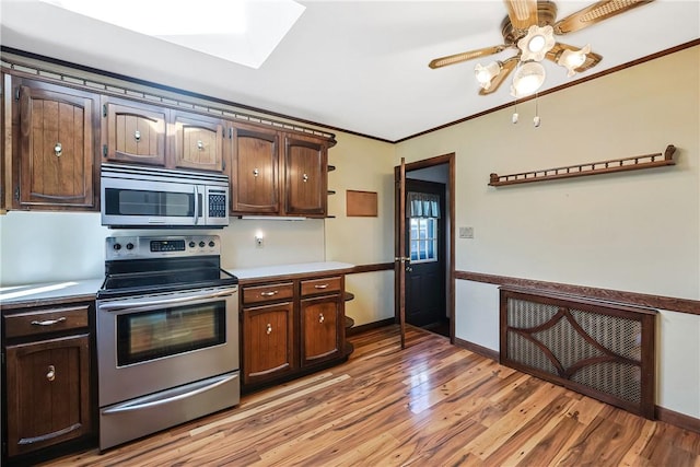 kitchen with light wood finished floors, appliances with stainless steel finishes, dark brown cabinetry, and crown molding