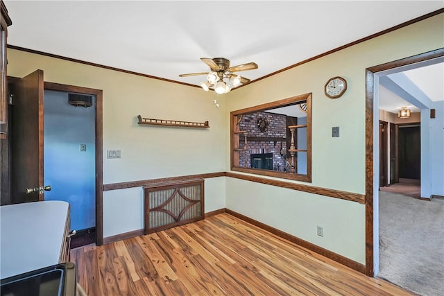 unfurnished dining area featuring ornamental molding, a ceiling fan, a brick fireplace, wood finished floors, and baseboards