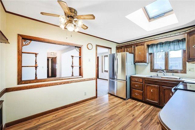 kitchen with crown molding, light wood finished floors, freestanding refrigerator, a sink, and range