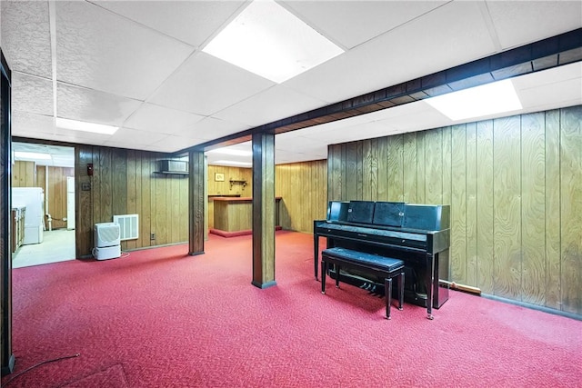 finished basement with carpet floors, a paneled ceiling, and wooden walls