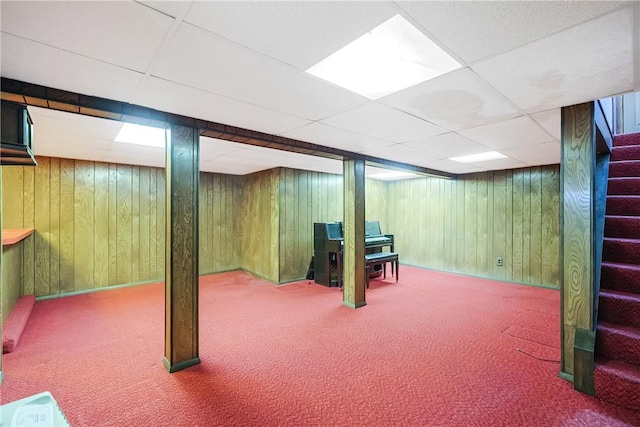 finished basement featuring carpet floors, wooden walls, and stairs