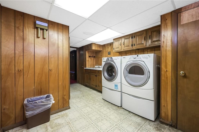 washroom featuring light floors, washing machine and clothes dryer, cabinet space, and wooden walls