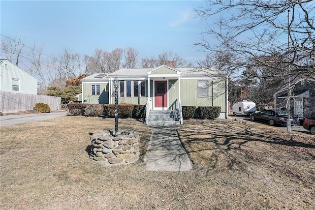 view of front facade with entry steps, a front lawn, a chimney, and fence