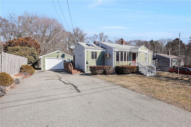 view of front of house with solar panels, a detached garage, aphalt driveway, fence, and an outdoor structure