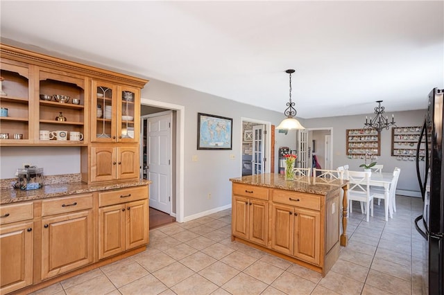 kitchen with pendant lighting, freestanding refrigerator, light tile patterned flooring, light stone countertops, and baseboards