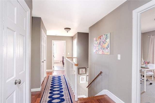 hall with baseboards, wood finished floors, and an upstairs landing