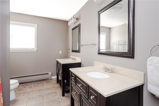 full bath with a baseboard heating unit, two vanities, a sink, and toilet