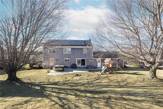 rear view of property with a lawn, a playground, a wooden deck, and roof mounted solar panels