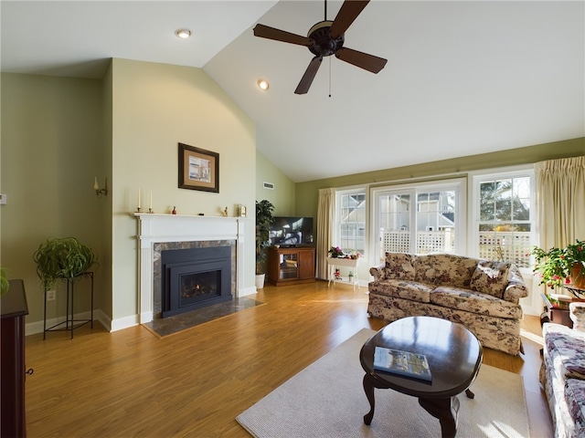 living room featuring ceiling fan, high vaulted ceiling, wood finished floors, a fireplace with flush hearth, and baseboards