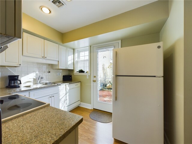 kitchen with white appliances, a sink, white cabinetry, visible vents, and decorative backsplash