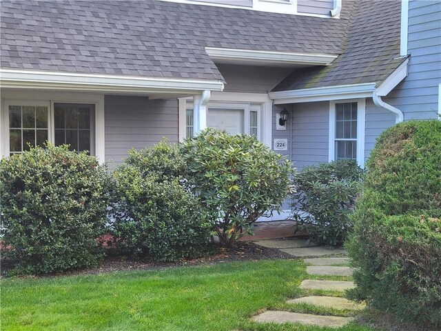 view of exterior entry featuring a shingled roof and a lawn