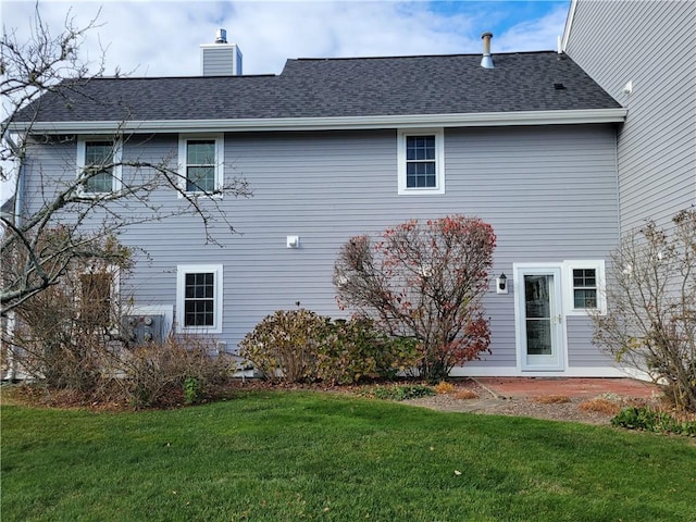 back of house with a shingled roof, a patio area, a yard, and a chimney