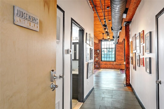 hallway with brick wall, wood finished floors, visible vents, and baseboards