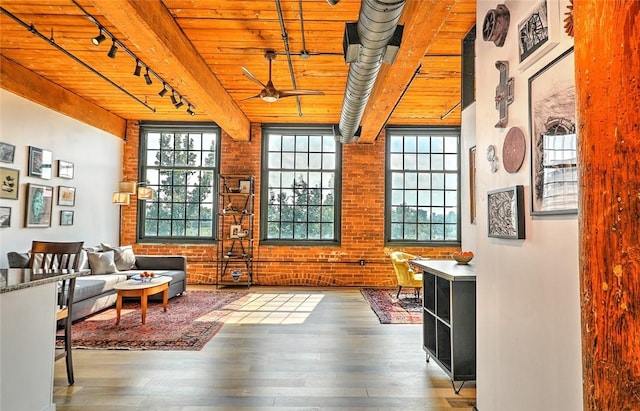 living area featuring a ceiling fan, rail lighting, brick wall, and wood finished floors