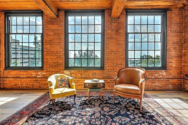 sitting room featuring brick wall, wood finished floors, and beam ceiling