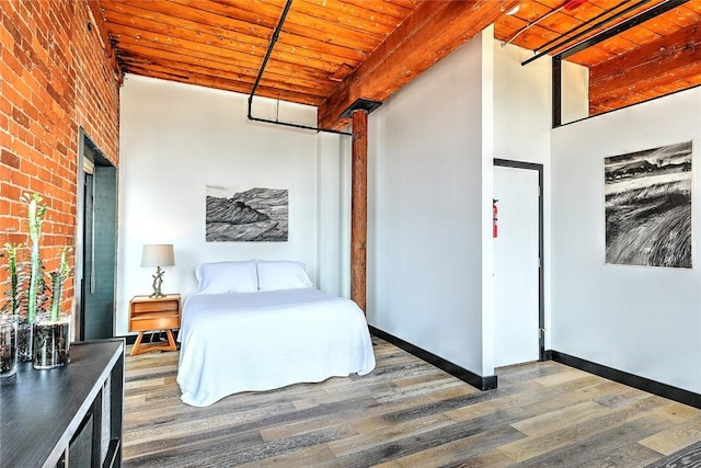 unfurnished bedroom featuring wood ceiling, brick wall, wood finished floors, beamed ceiling, and baseboards