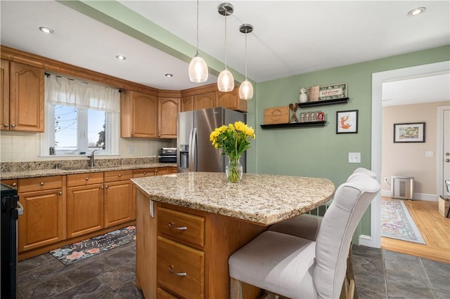 kitchen with a kitchen island, backsplash, a sink, and stainless steel fridge with ice dispenser