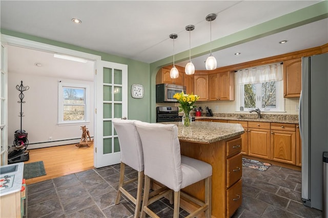 kitchen with a kitchen island, appliances with stainless steel finishes, stone finish flooring, baseboard heating, and a kitchen bar